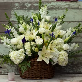 White lilies and roses in a wicker basket with blue iris accents