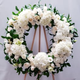 White floral wreath with roses and hydrangeas on a wooden stand