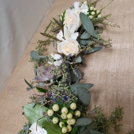 White roses and succulents arranged with eucalyptus and berries on burlap