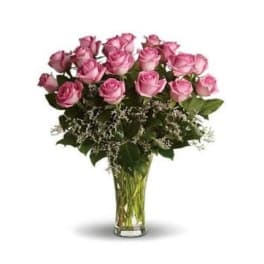 Tall arrangement of pink roses with white filler flowers in a clear glass vase