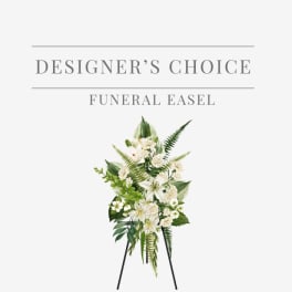 White funeral standing spray with lilies and other blooms on a black easel stand