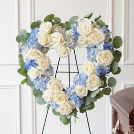 Heart-shaped floral wreath of white roses and blue hydrangeas on a stand