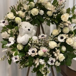 White floral wreath on an easel with a plush teddy bear in the center