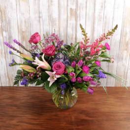 Pink and purple mixed flower arrangement with lilies and roses in a round glass vase