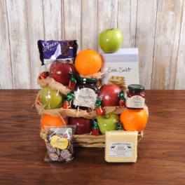 Gift basket with apples, oranges, jams, cheese, chocolates, and crackers on a wooden table.