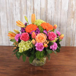 Bright mixed bouquet of orange, pink, and peach flowers in a clear glass vase