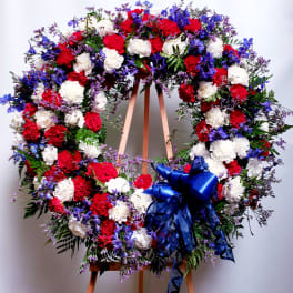 Large red, white, and blue floral wreath on an easel with a ribbon bow