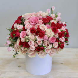 Large arrangement of red and pink roses with tulips in a white cylinder vase