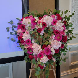Heart-shaped floral arrangement with pink roses, hydrangeas, and gerbera daisies on an easel