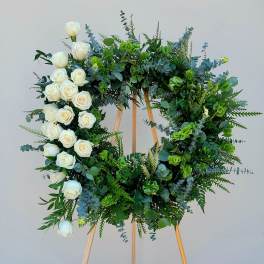Circular floral wreath of white roses and mixed greenery on a wooden easel