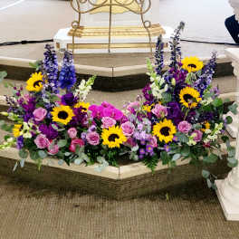 Two floral sprays with sunflowers, pink roses, and purple blooms on a church step