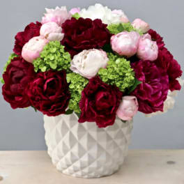 Red and pink peonies with green hydrangeas in a white vase