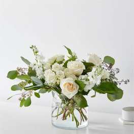 White roses and white blooms in a clear glass vase with greenery