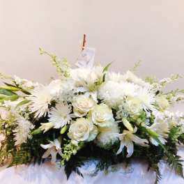 White floral casket spray with roses, lilies, and chrysanthemums