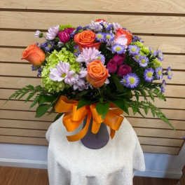 Bouquet of orange roses and purple daisies in a vase with an orange ribbon