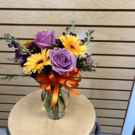 Bouquet of purple roses and yellow gerbera daisies in a glass vase