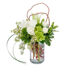 White roses and green flowers arranged in a glass vase with curly branches