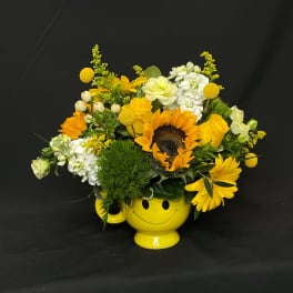 Yellow flower arrangement in a smiley-face mug