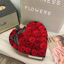 Heart-shaped box filled with red roses and a ribbon bow