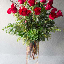Red roses arranged in a clear glass vase with greenery and a succulent accent