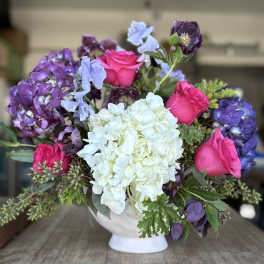 Bouquet of pink roses, white hydrangea, and purple blooms in a white vase
