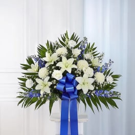 White floral standing spray with a blue ribbon on a pedestal