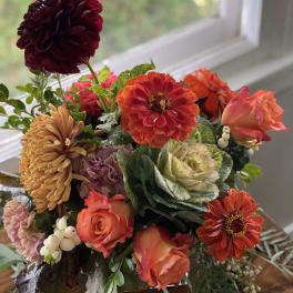 Mixed bouquet of orange, pink, and burgundy flowers in a vase