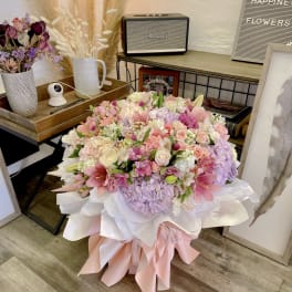 Large pastel bouquet of pink, white, and lavender flowers wrapped in white and pink paper