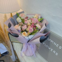 Pastel bouquet of pink and peach roses with mixed blooms in lavender wrap