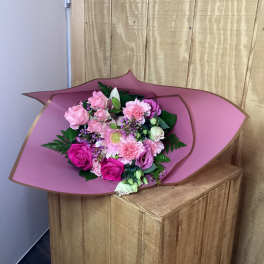 Pink bouquet with roses, carnations, and a daisy-like bloom wrapped in mauve paper