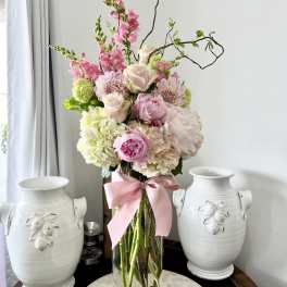 Tall pink and white floral arrangement in a clear glass vase with a pink ribbon