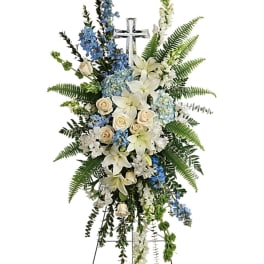 Standing funeral spray with white lilies, cream roses, and blue flowers on a cross stand