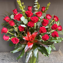 Red roses arranged in a clear glass vase with tropical foliage