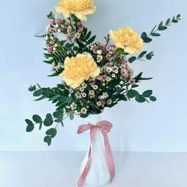 Yellow flowers in a white vase with a pink ribbon