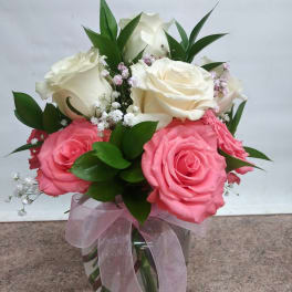 Pink and white roses arranged in a glass vase with a pink ribbon