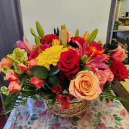 Mixed bouquet of roses, lilies, and a yellow gerbera daisy in a wicker basket