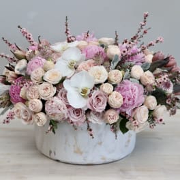 Low arrangement of blush roses, pink peonies, and white orchids in a round white ceramic vase