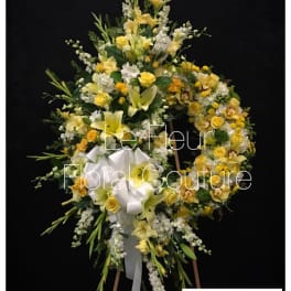 Yellow and white floral funeral wreath on an easel with a white ribbon
