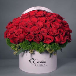 Red roses arranged in a round pink hat box with green filler at the base