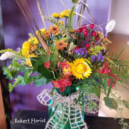 Mixed bouquet in a teal glass vase with yellow and orange flowers
