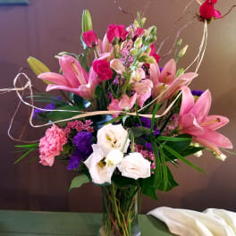 Pink lilies, roses, and white blooms arranged in a glass vase