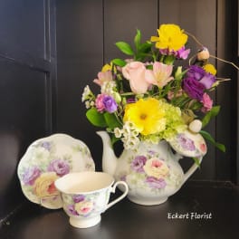 Floral arrangement in a floral teapot with matching teacup and saucer