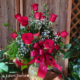 Red roses arranged in a clear glass vase with a red ribbon bow