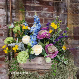 Mixed floral arrangement in a wooden box with blue, pink, yellow, and white blooms