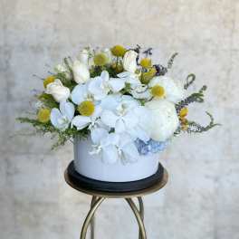 White orchids and roses in a round white vase with yellow accents