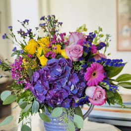 Colorful bouquet with purple hydrangea, pink roses, yellow roses, and a pink gerbera daisy in a vase