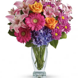 Mixed bouquet of pink, purple, and orange flowers in a clear glass vase