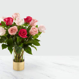 Pink and red roses arranged in a clear vase with a gold sleeve