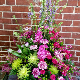 Tall basket arrangement with pink blooms, green spider mums, purple delphinium, and tulips
