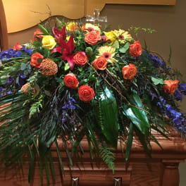 Large casket spray with orange and yellow roses and purple flowers